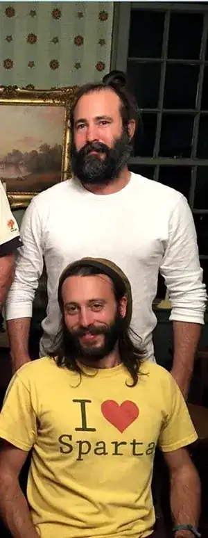 Jim Baker standing behind his younger brother David Baker, who is seated wearing a yellow I Love Sparta t-shirt