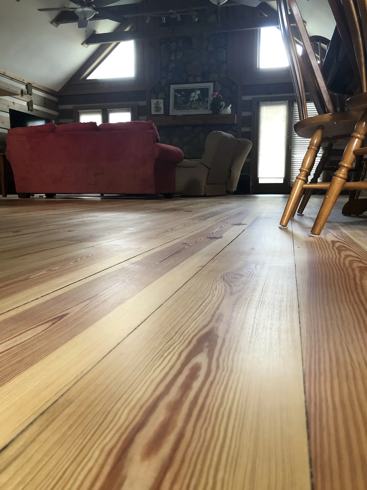 Wide-plank antique heart pine floor glowing in a timber-framed great room with a stone fireplace