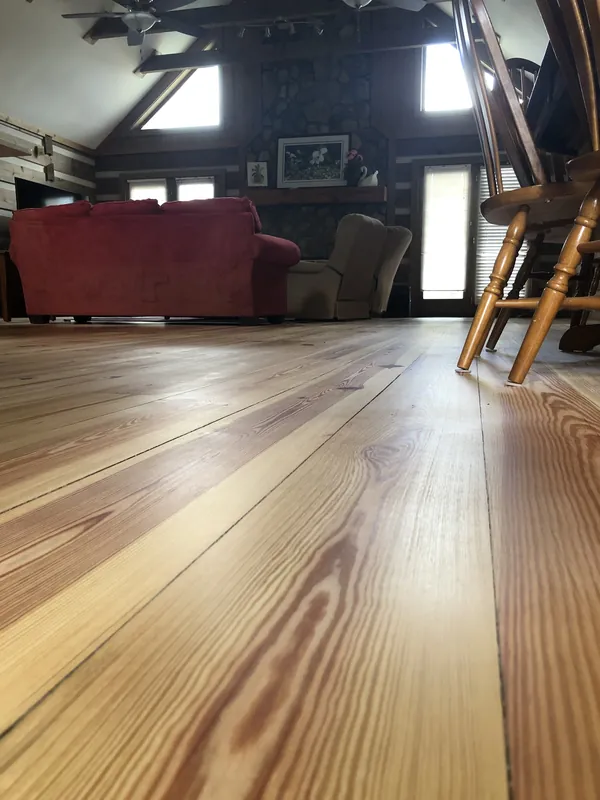 Wide-plank antique heart pine floor with amber grain glowing in a log great room with a stone fireplace