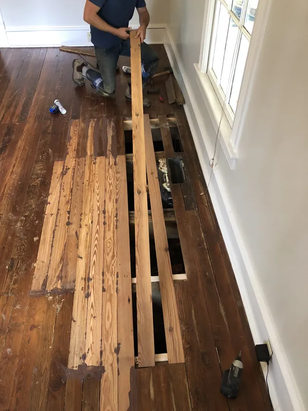 Craftsman fitting a new heart pine board into a partially replaced antique pine floor near a skylight