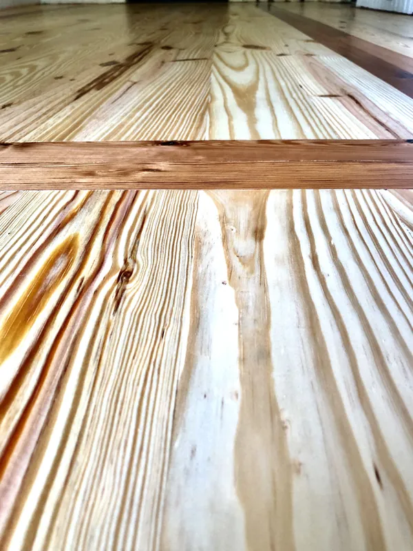 Close-up of glossy heart pine floorboards meeting a contrasting inlaid border strip