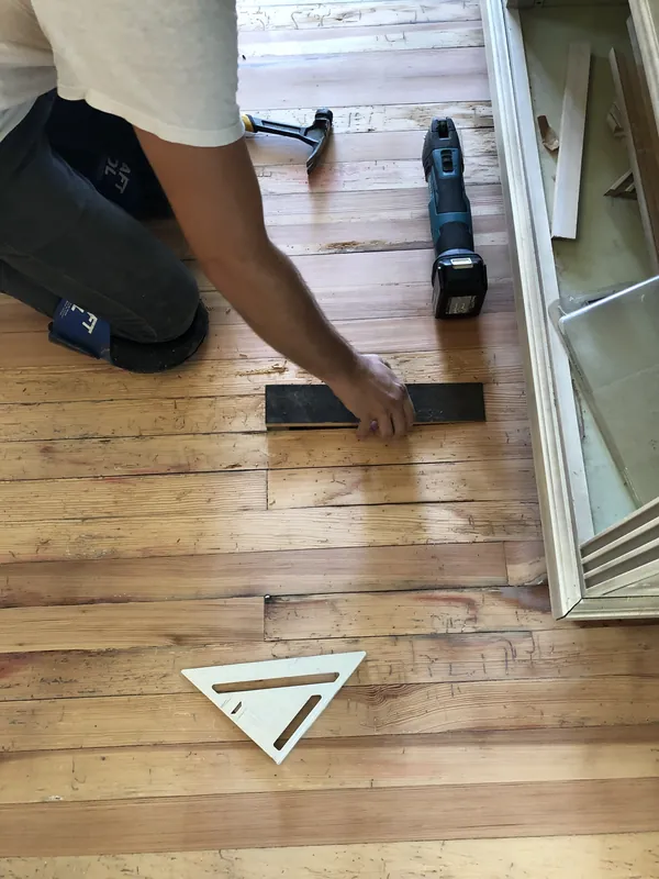Craftsman using a square and saw to fit a new dark board into a worn antique pine floor