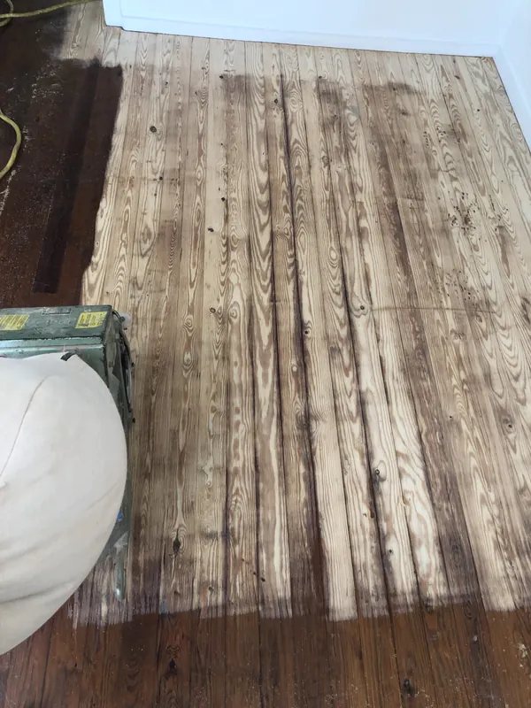 Old wide-plank heart pine floor partially sanded showing lighter fresh wood against darker finish