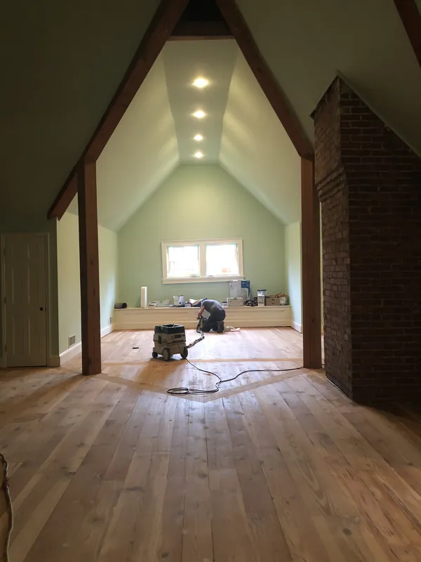 Craftsman installing light wood plank floor in a vaulted room with an exposed-beam ceiling