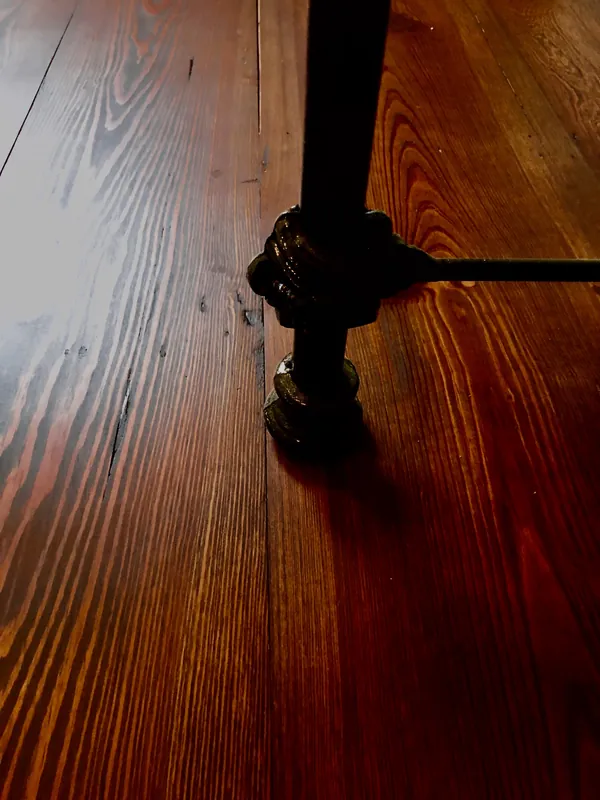 Glossy dark-stained heart pine floor with a black metal furniture leg and finial