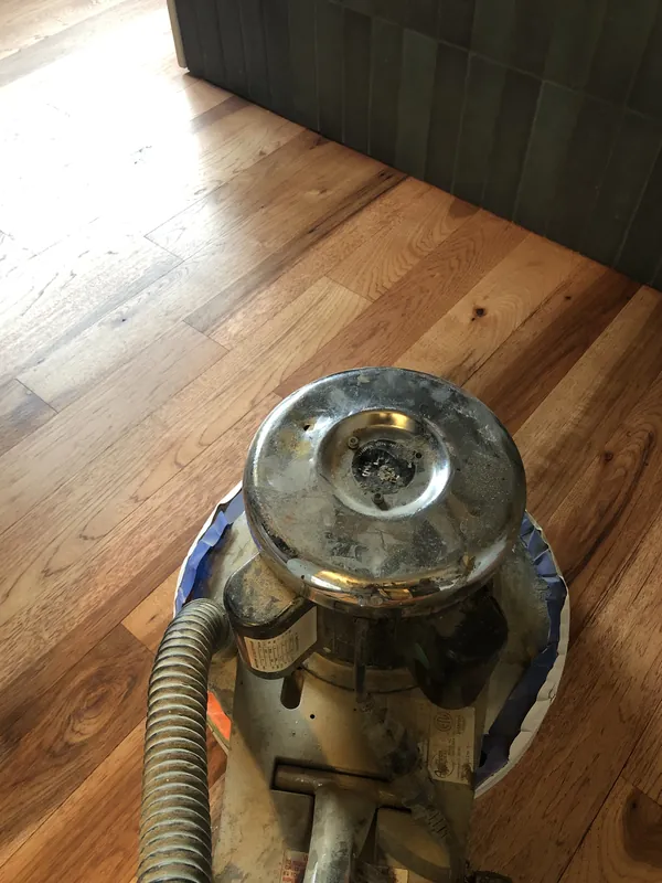 Floor drum sander sitting on partially sanded oak strip flooring