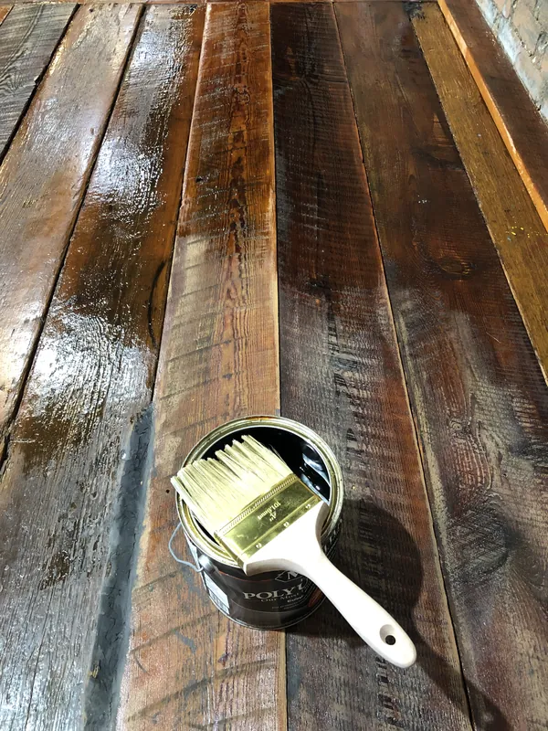 Brush resting on a finish can atop freshly coated dark reclaimed pine planks