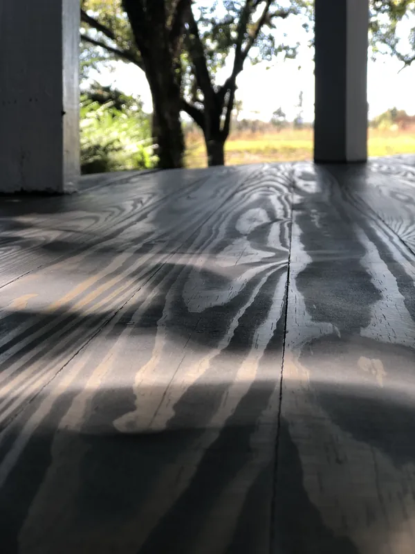 Low-angle grey plank porch floor with dappled shadows framed by posts opening to trees