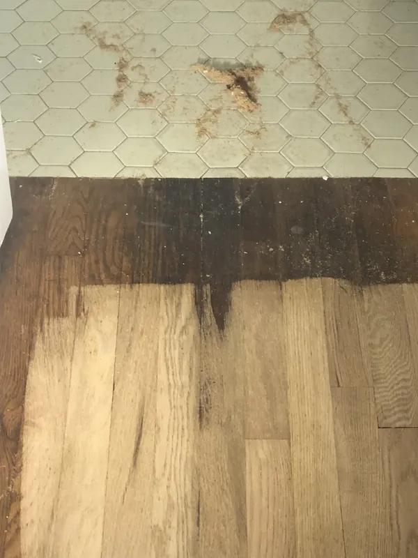 Oak floor half stripped of dark finish next to a hexagonal tile floor