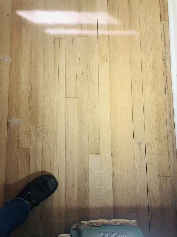 Bare sanded oak strip floor with a boot at left and a Lägler edge sander at the bottom of the frame