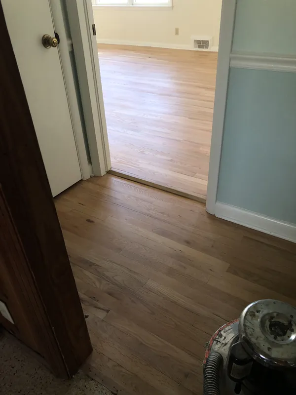 Newly installed light oak flooring meeting painted trim and a wood threshold in a doorway
