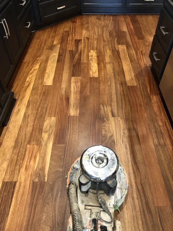 Rotary buffer on a glossy warm-brown wood floor flanked by dark navy cabinetry