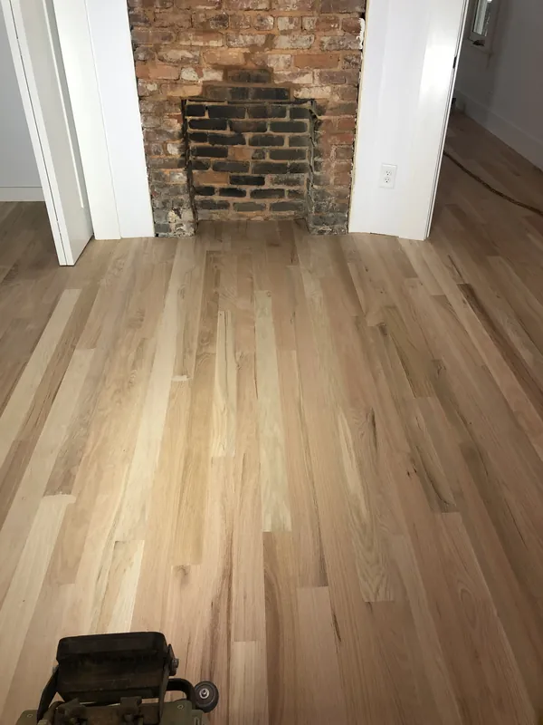 Newly installed pale white oak flooring running up to a rugged exposed brick fireplace