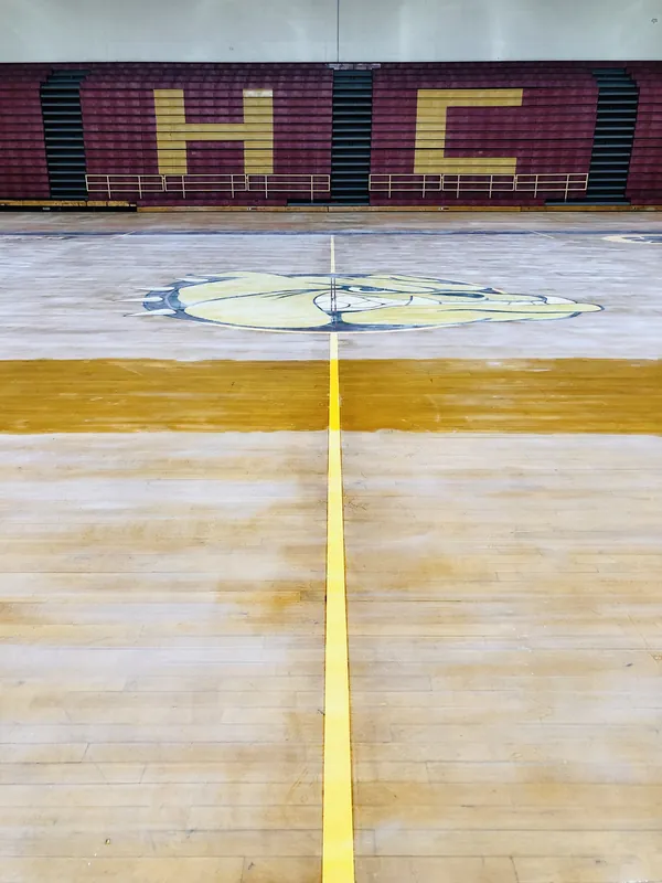 Empty gymnasium basketball court with maple floor, painted lines, a bulldog logo and bleachers