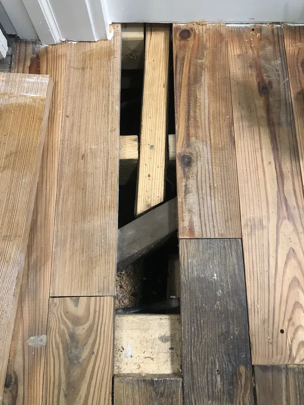 Close-up of reclaimed heart pine boards being fitted, with a gap exposing the subfloor framing