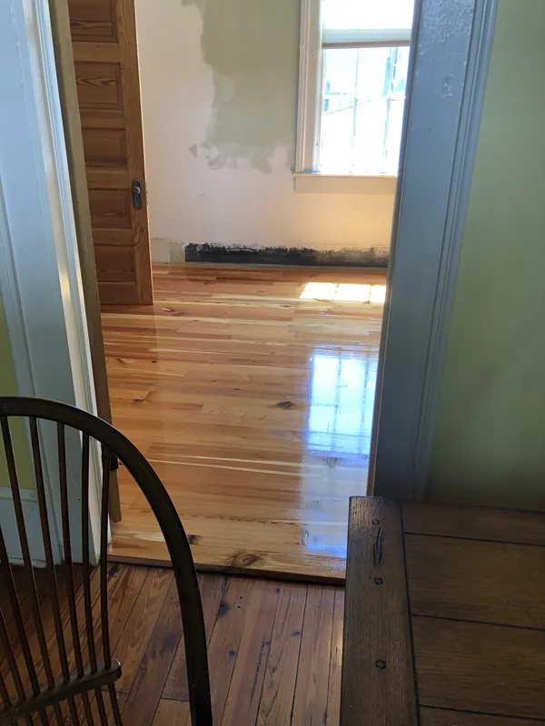 Freshly installed pale heart pine wall paneling beside older dark boards and painted trim