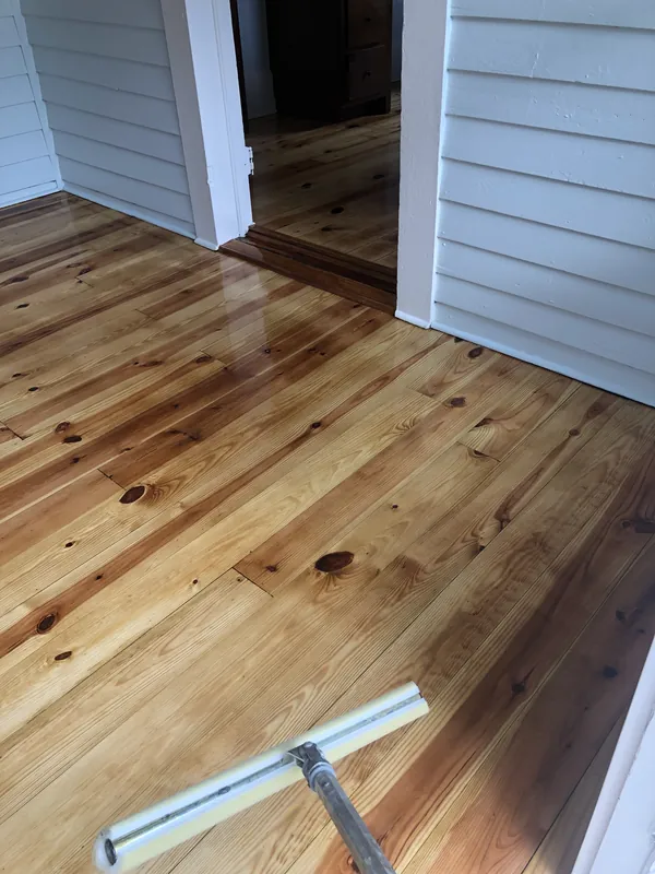 Freshly finished honey pine plank floor with a T-bar applicator beside white beadboard cabinetry