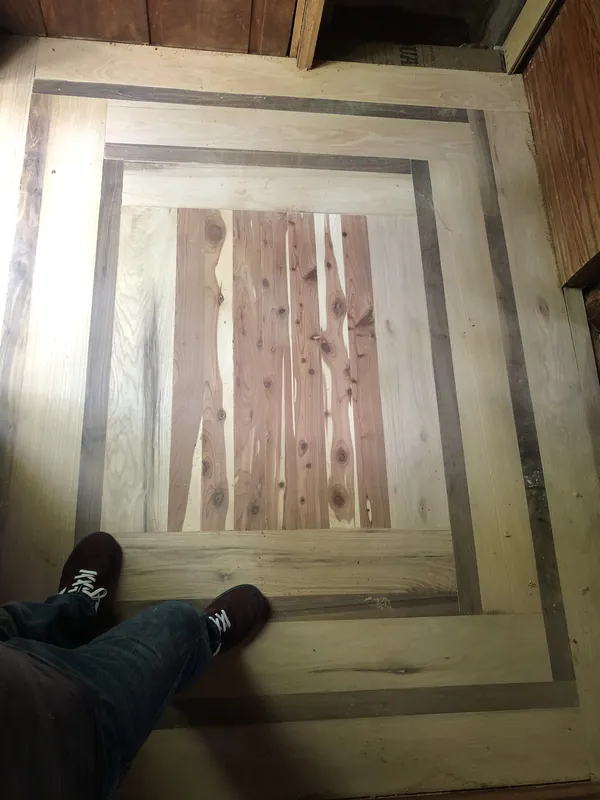 Overhead view of a square parquet-style floor inset with contrasting border bands and a cedar center