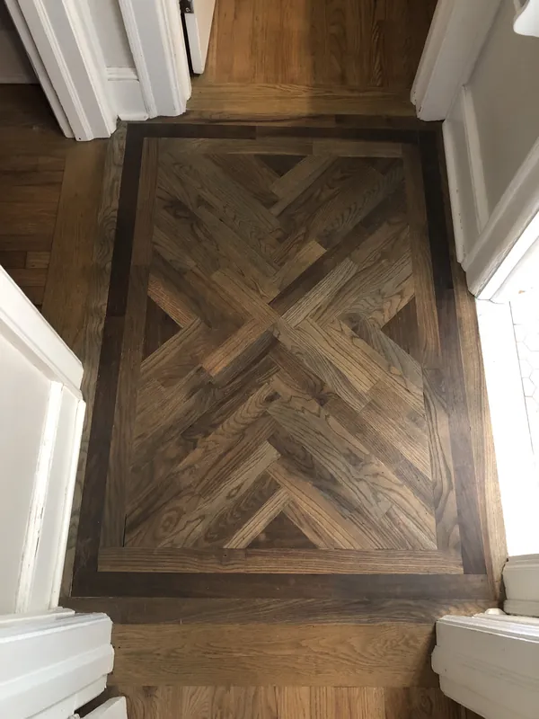 Geometric oak parquet inlay panel with an X pattern and dark framed border set in a floor