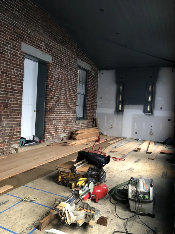 Gut-renovation room with an exposed brick wall, loose flooring planks staged over building paper and tools