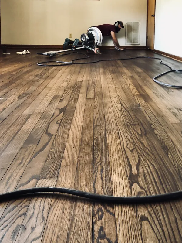 Low-angle view of stained red oak strip floor with a craftsman buffing at the far wall