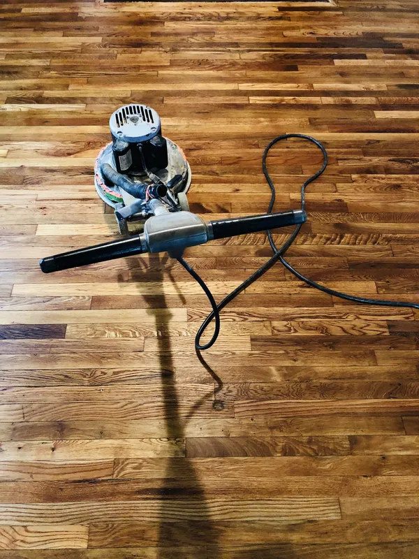 Black-and-white photo of a drum sander on antique pine as a craftsman kneels by exposed brick