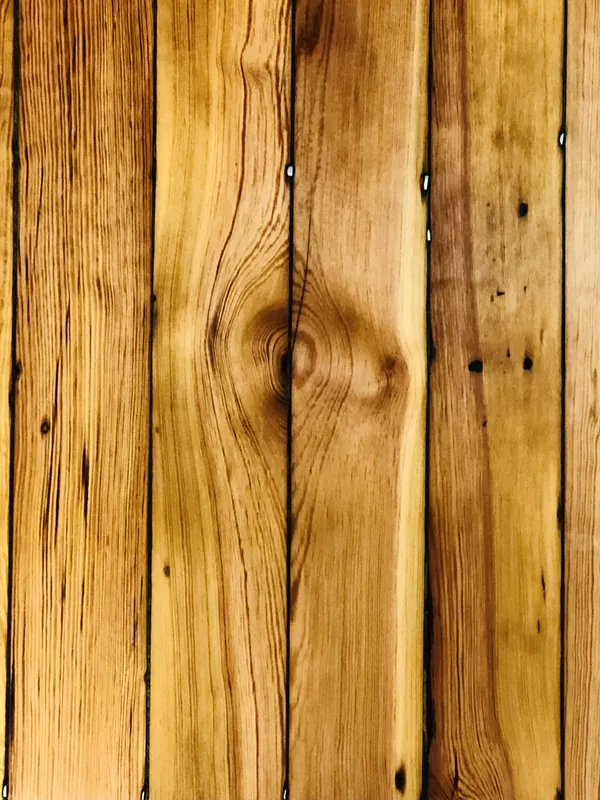 Close-up of warm honey-toned vertical heart pine boards showing tight grain, a knot and old nail holes