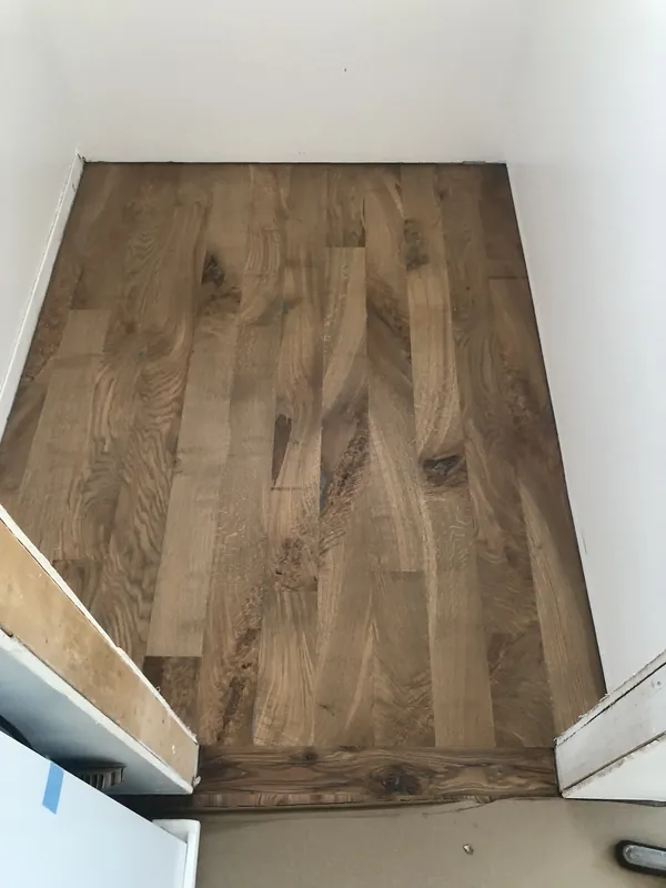 Small room with newly finished light oak plank floor meeting white baseboards