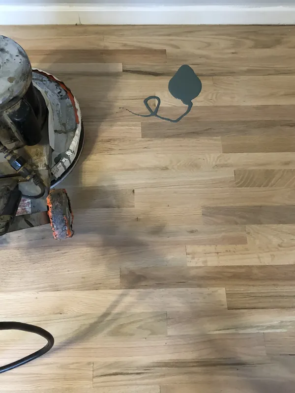 Handheld edge sander on light unfinished white oak flooring near a doorway